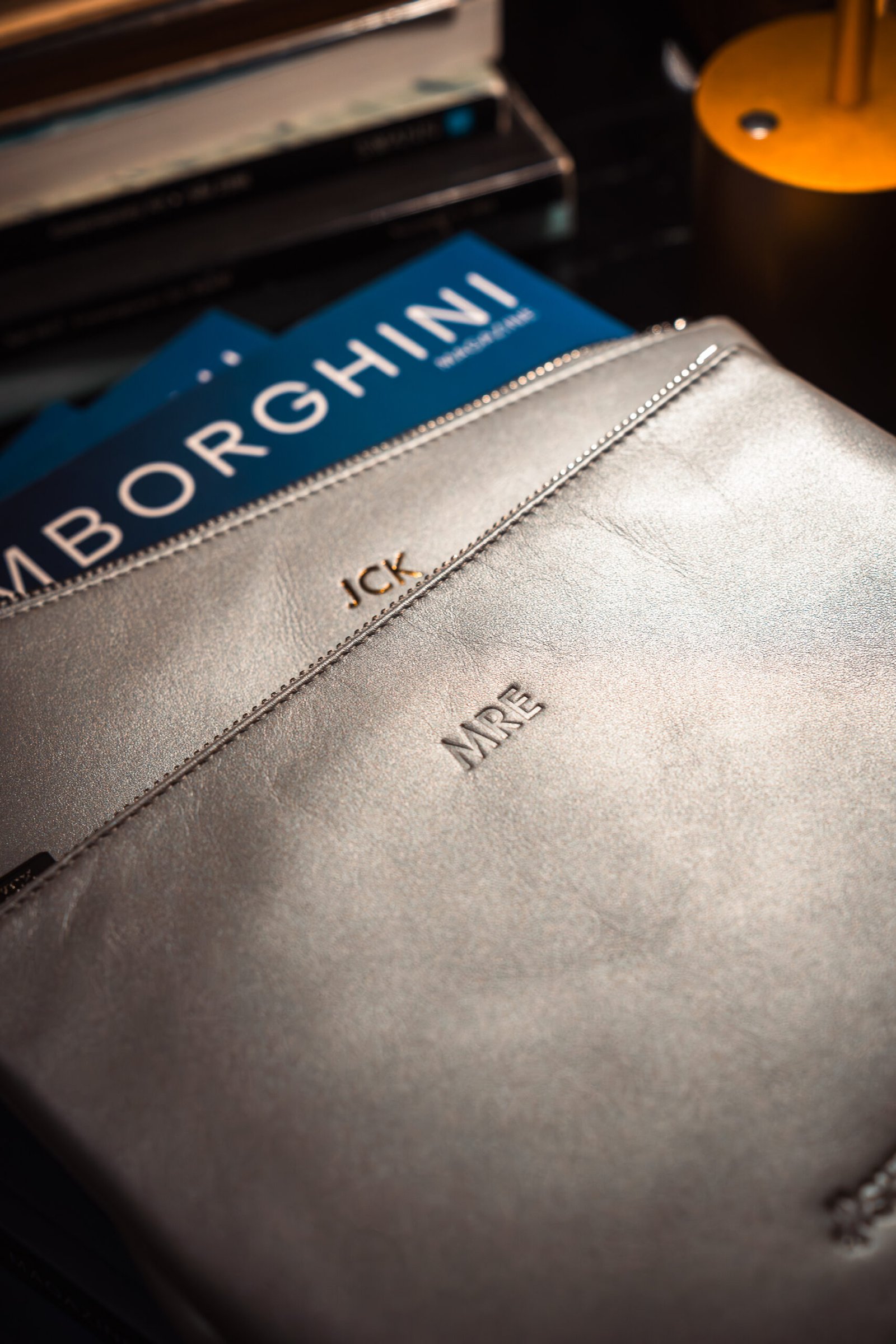 Lamborghini SheDrives: Personalization for a Powerful Driving Experience Two white vegan leather license plate keychains from Prime Video’s Maintenance Required premiere, one embossed with KU in dark blue foil and the other showing the debossed “Maintenance Required” and “Prime Video” logos.