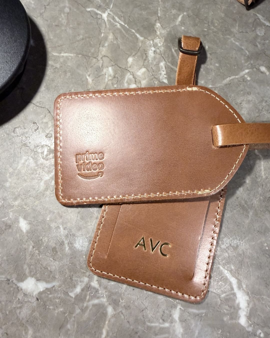 Prime Video CES Party Luggage Tag Two white vegan leather license plate keychains from Prime Video’s Maintenance Required premiere, one embossed with KU in dark blue foil and the other showing the debossed “Maintenance Required” and “Prime Video” logos.